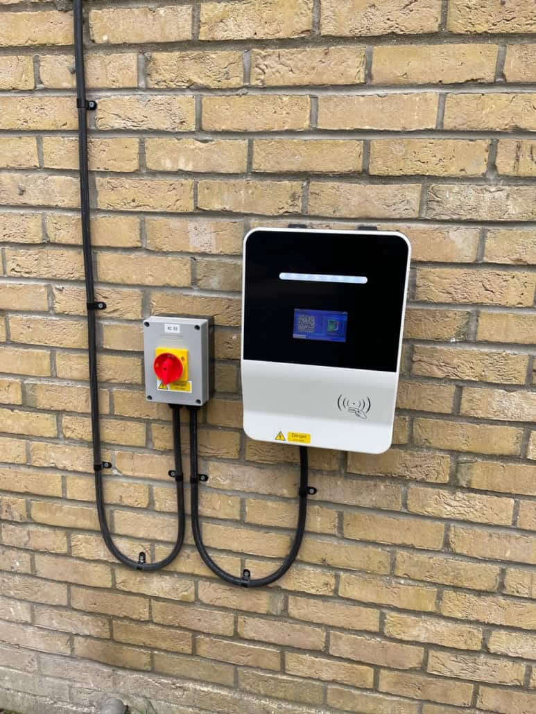 EV charger and a control unit mounted on a brick wall, with black cabling connecting both devices.